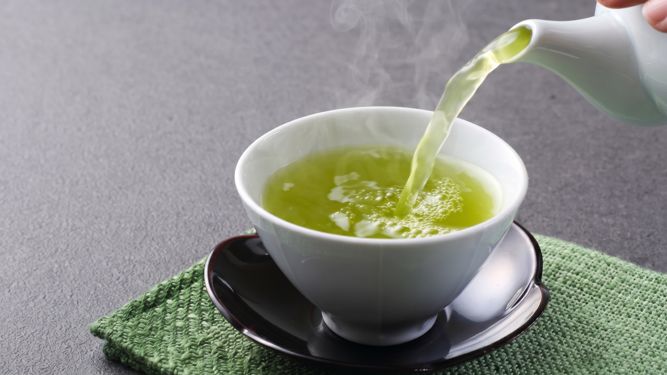 10 Sleep Aids That Actually Work: Science-Backed Options For Better Rest 7 A Steaming Stream Of Vibrant Yellow-Green Green Tea Pours From A White Ceramic Teapot Into A White Cup. The Cup Sits On A Dark Saucer And A Textured Green Placemat Over A Grey Counter