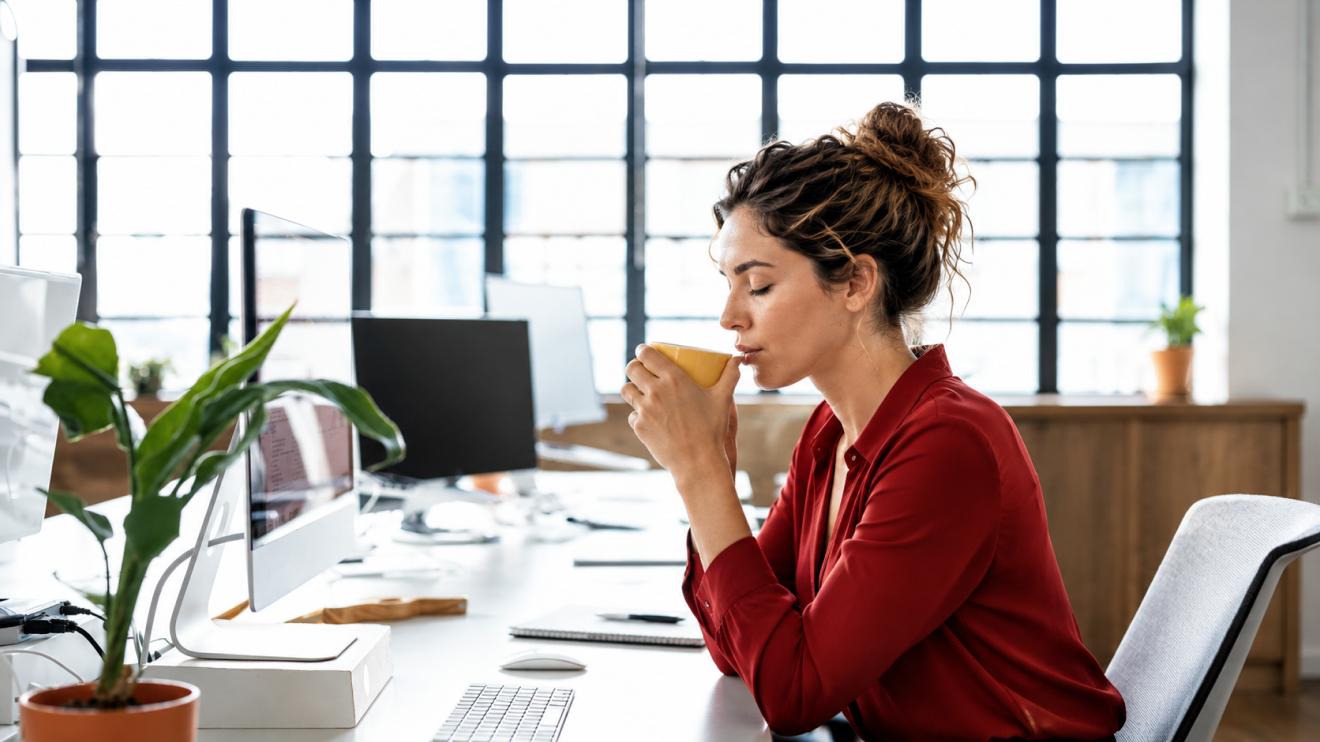6 Healthy Habits For A Clearer, More Focused Day 5 A Woman Pauses At Her Desk With A Warm Drink In A Bright Office, Illustrating A Small Moment Of Calm And Awareness During A Busy Workday.