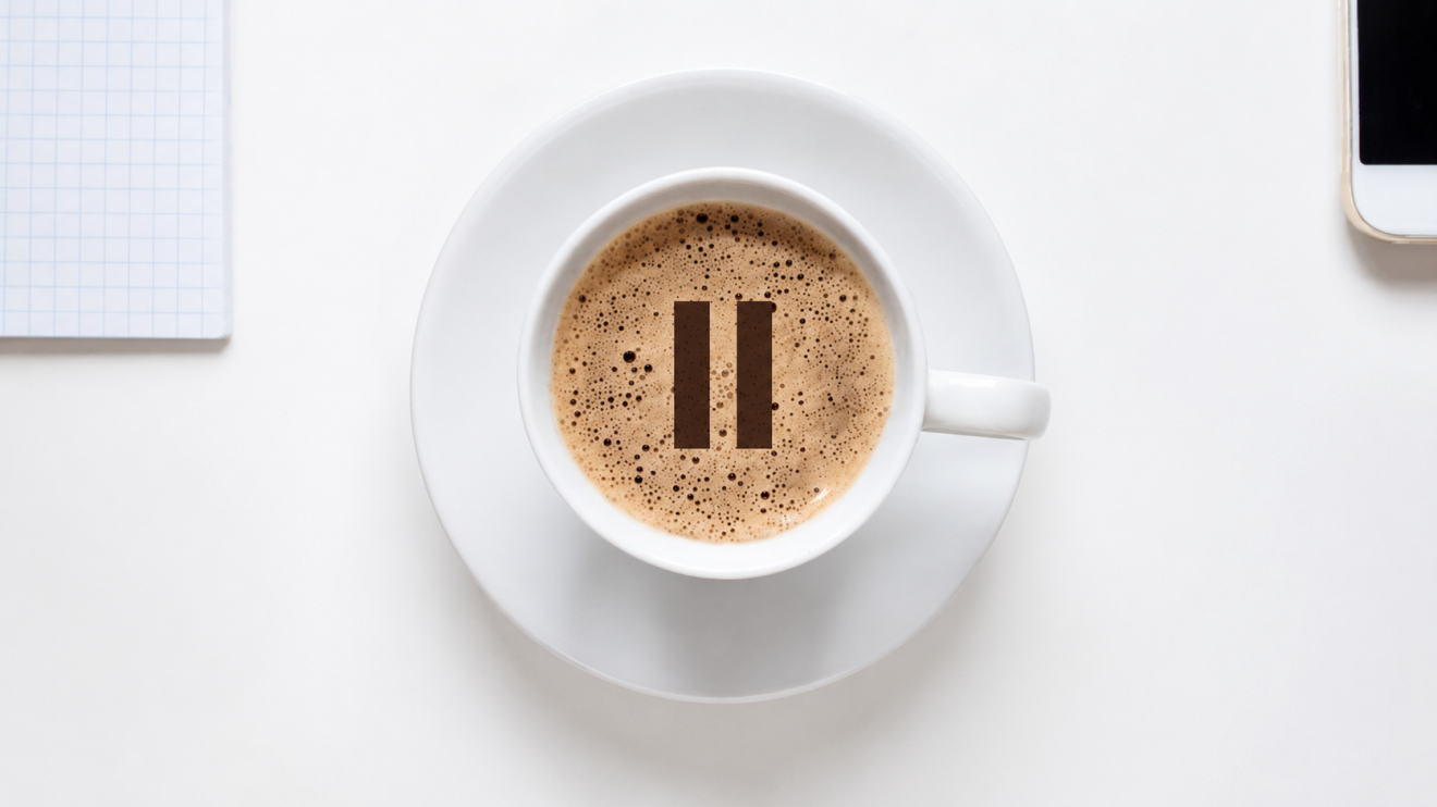 The Deep Focus Routine: 6 Proven Ways To Build It 7 Top-Down View Of A White Coffee Cup On A White Table With A Pause Symbol In The Foam, Next To A Notebook And Smartphone In A Minimalist Workspace.