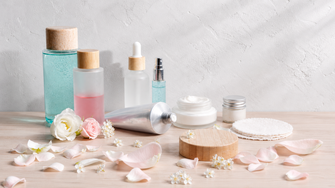 Why Your Skin Looks Tired: 9 Hidden Causes &Amp; Quick Fixes 8 A Flat Lay Of Assorted Skincare Products And Creams Arranged On A Table With Flowers And Petals, Representing An Overloaded Skincare Routine Where Using Too Many Products May Harm The Skin Instead Of Helping It.