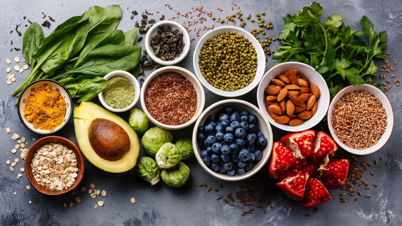 Morning Glow Routine: 8 Daily Habits For Radiant Skin 4 A Vibrant Flat-Lay Photograph Showcases An Array Of Antioxidant-Rich Superfoods On A Grey Slate Background, Emphasizing A Nutrient-Dense, Plant-Based Diet. The Arrangement Includes Colorful Fresh Produce Like Blueberries, Pomegranate, And Avocado Alongside Leafy Greens Like Spinach And Parsley. Bowls Of Almonds, Flaxseeds, And Mung Beans Provide Healthy Fats And Fiber, While Turmeric, Matcha, And Loose-Leaf Tea Offer Concentrated Antioxidants.