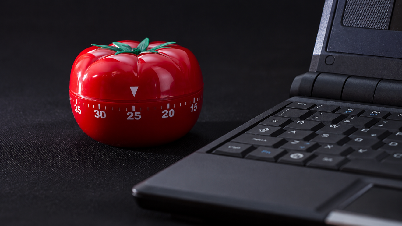 Low Energy Day Routine: 9 Steps That Still Get Results 7 Tomato-Shaped Kitchen Timer Beside A Laptop On A Dark Desk, Symbolizing The Pomodoro Technique And The Idea Of Working In Short, Focused Intervals Instead Of Forcing Hours Of Exhausting Concentration On Low-Energy Days.