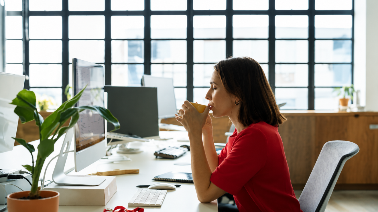 Low Energy Day Routine: 9 Steps That Still Get Results 9 Woman Pausing At Her Desk With A Warm Drink In A Bright Workspace, Taking A Quiet Moment Away From Active Work To Recharge. The Scene Emphasizes The Importance Of Taking Small Breaks Throughout The Workday Before Mental Fatigue Builds Up And Makes It Difficult To Focus Or Stay Productive.