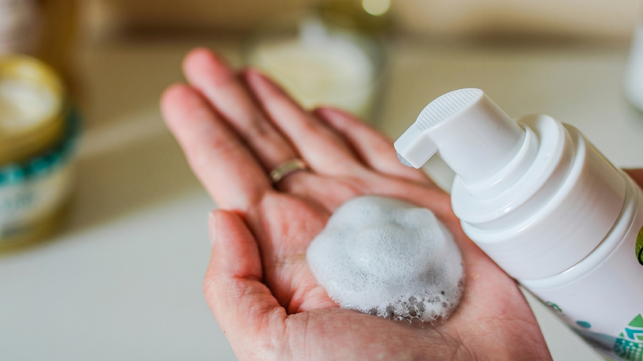 Morning Glow Routine: 8 Daily Habits For Radiant Skin 2 A Person Holds Their Palm Open, Catching A Dollop Of White Foaming Cleanser Being Dispensed From A White Pump Bottle.